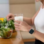 Young woman eating healthy salad and drinking milk after workout